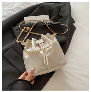 Detailed view of floral embroidery on cream bucket bag with pearl handle and chain strap