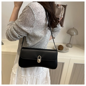 Close-up of minimalist black underarm bag with gold oval buckle and smooth finish