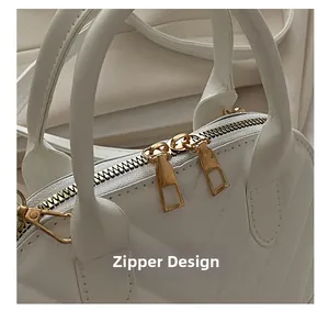 Detail of white V-quilted handbag showing dual gold zipper closure and synthetic leather texture