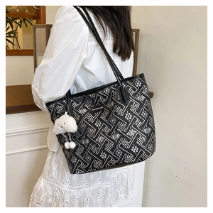 Black tote bag with geometric print and cloud pendant worn by a model in a white dress