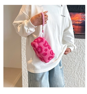 Detalle de bolsa de cosméticos de felpa rosa con textura de corazones 3D y asa