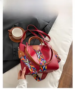 Detail of red leather handbag with colorful woven shoulder strap and round handle
