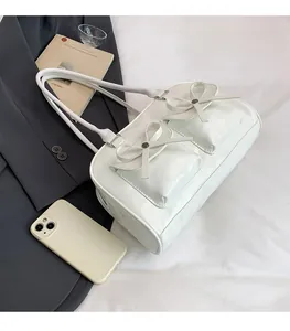 Detail of a creamy white Boston bag with bow pockets next to a phone for scale