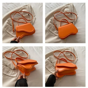 Detail view of bright orange leather handbag with unique wavy bottom and slim shoulder strap