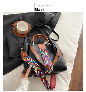 Close-up of black handbag featuring ethnic geometric woven strap and brown leather handle