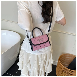Detail of pink heart-patterned crossbody bag with silver bow and black top handle