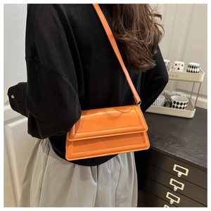 Detail of orange quilted leather crossbody bag with flap cover on a female model