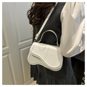 Detail of white saddle bag showing wavy curve flap and golden metallic buckle