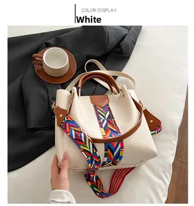 Detail view of white bucket bag with brown handle and patterned strap in urban setting