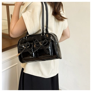 Detail of glossy black shoulder bag with ballet style bows and double flap pockets