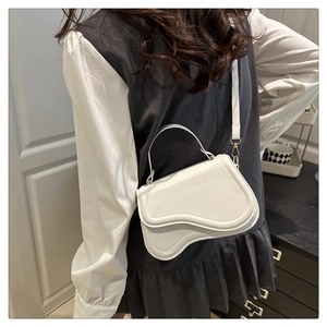 Detailed view of the asymmetrical curved flap and gold-tone buckle on white saddle bag