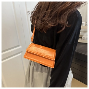 Detail of bright orange leather shoulder bag with fine stitching and gold metal buckle