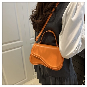 Detail of a bright orange saddle bag with wavy flap and adjustable shoulder strap on model