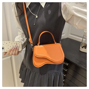 Close-up of bright orange wave-flap crossbody bag with smooth leather texture