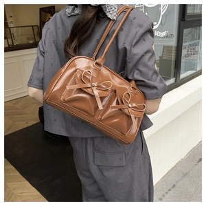 Detail of caramel leather shoulder bag featuring ribbon bows and twin accordion pockets