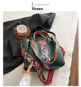 Detail of dark green handbag featuring brown handles and geometric patterned shoulder strap