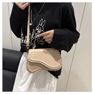 Detail view of a beige saddle bag with adjustable shoulder strap worn by a model