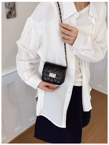 Detail of black quilted crossbody bag with gold twist lock and chain strap on model