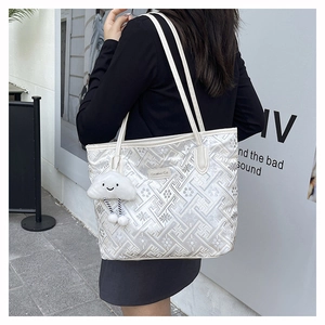 White tote bag detail featuring geometric floral embroidery and a plush cloud charm on a model