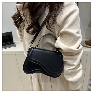 Side view of a black saddle bag with wavy flap and gold hardware on a woman's shoulder