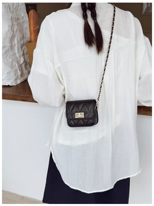 Detail of black quilted mini bag with gold twist lock and chain strap on white shirt