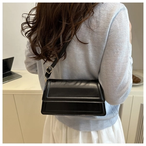 Detail of minimalist black crossbody bag showing smooth faux leather texture and gold hardware