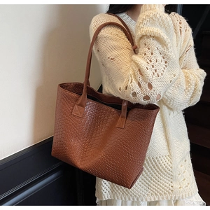 Detail of a brown tote bag featuring a woven texture and slender shoulder straps