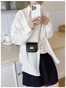 Détail du sac matelassé noir à chaîne avec fermoir doré sur fond de chemise blanche