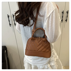 Detail showing the brown V-quilted texture and gold zipper of the shell-shaped handbag