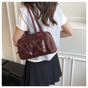 Detail of burgundy glossy faux leather Boston bag with bow pockets on white t-shirt