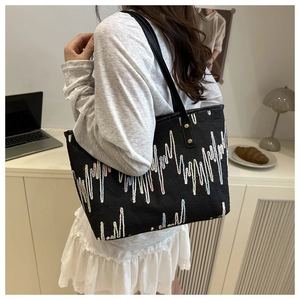 Detail of a black tote bag with colorful wave embroidery worn by a model in a modern office