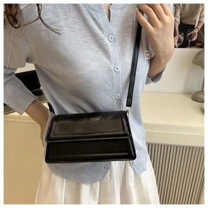 Close-up of minimalist black crossbody flap bag with quilted texture shown on a model