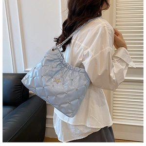 Close-up of light blue quilted bucket bag with star rivet and silver chain strap