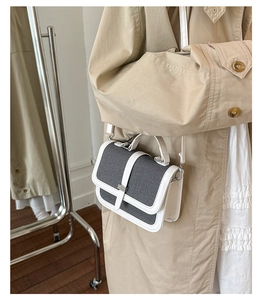 Side view of woman in beige trench coat carrying a grey canvas crossbody bag with white trim