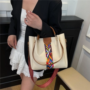 Chic beige tote bag with woven color stripes and broad shoulder strap on model