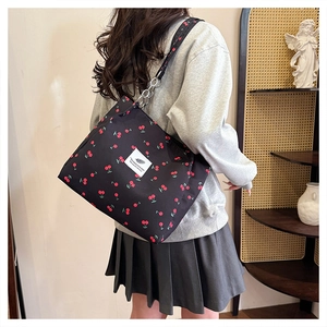 Detail of black canvas tote bag with red cherry prints and silver chain buckle attachment