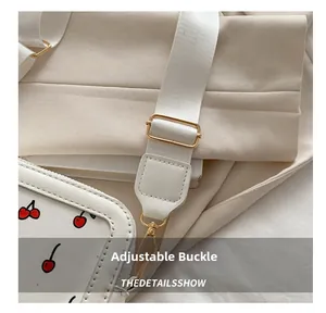 Close-up of adjustable golden buckle and cherry print leather detail on a white bag