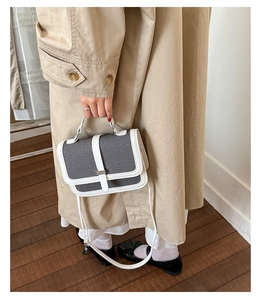 Detailed shot of grey canvas crossbody bag with white leather trim held by a model