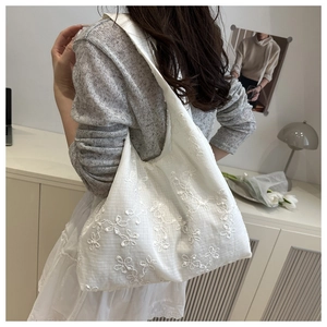 Detail of white floral embroidery on translucent mesh fabric of a stylish tote bag