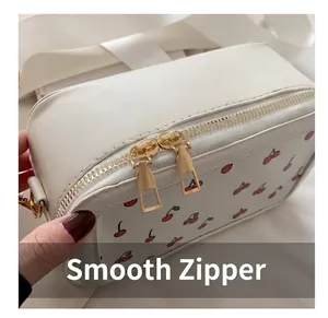 Detalle de cremalleras doradas y estampado de cerezas en el bolso bandolera blanco