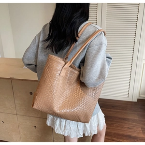 Detail of light brown woven texture tote bag worn on shoulder by a model in soft light