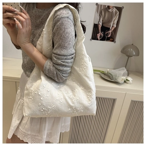Detailed side view of white tote bag with floral embroidery on soft fabric