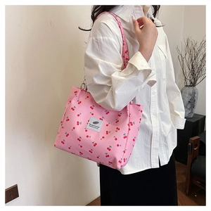 Close-up of pink tote bag with cherry print and decorative logo patch on fabric