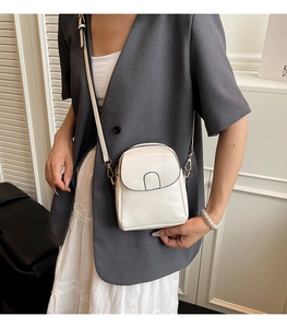 Detail of a white mini faux leather crossbody bag with gold hardware and adjustable strap