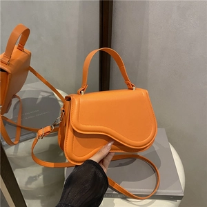 Vibrant orange saddle-style handbag with wave-curved flap and adjustable crossbody strap