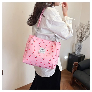 Detail of pink cherry print tote bag featuring a decorative fabric label and metal chain link