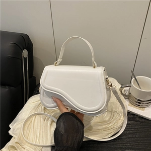 Minimalist white saddle handbag with gold clasp and adjustable strap on a wooden table