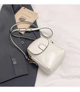 Close-up of a white leather crossbody bag with adjustable strap and gold metal buckles