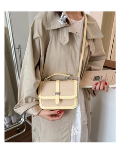 Model wearing a beige woven crossbody bag with leather trim and silver metal buckle detail