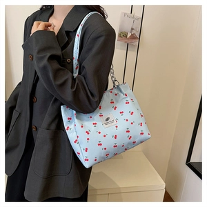 Detail of light blue cherry print tote bag with metallic chain and woven shoulder strap
